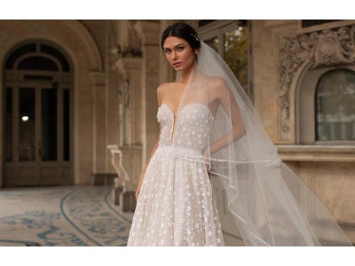 Brunette woman wearing a sweetheart neckline wedding dress with floral appliqués and a long veil.