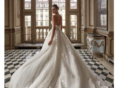 Brunette woman in a ball gown wedding dress standing in a ball room and looking back at the camera.