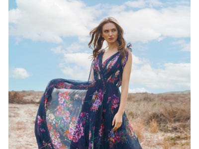 Blonde-haired woman wearing a floral formal gown with a v neckline and standing on the beach.