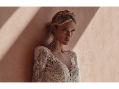 Bride with natural bride make up in a lace wedding dress leaning against a wall