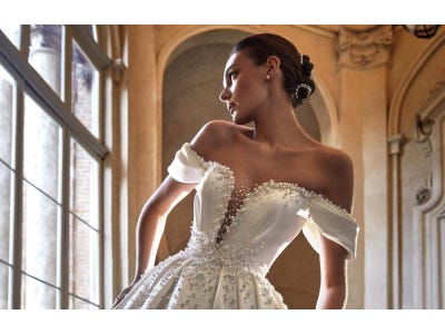 Woman in an off-the-shoulder bridal gown with intricate beading along the neckline and hair in a low bun.