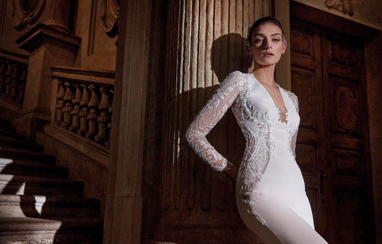 Mujer apoyada sobre una columna con el pelo recogido y un vestido de novia con escote en pico.