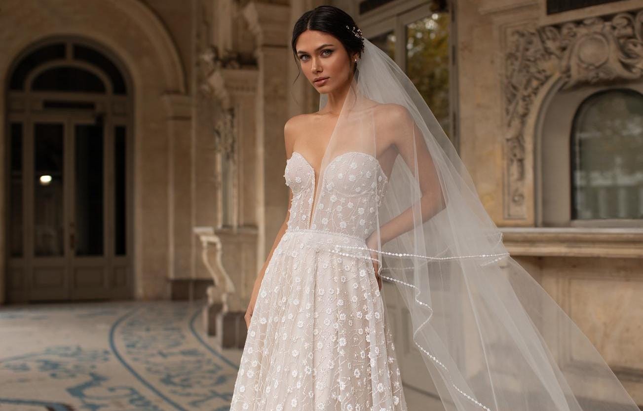 Brunette woman wearing a sweetheart neckline wedding dress with floral appliqués and a long veil.