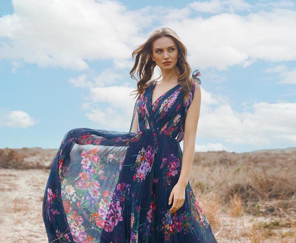 Blonde-haired woman wearing a floral formal gown with a v neckline and standing on the beach.