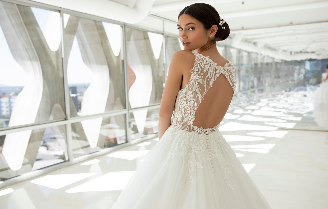 Brunette woman with a bun wedding hairstyle is standing in a corridor looking back at the camera. 