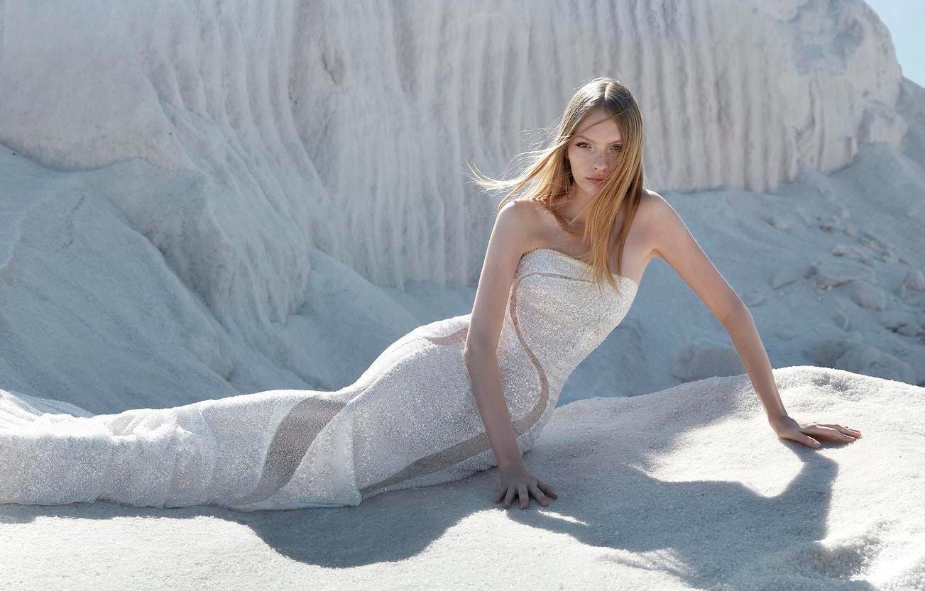 Noiva de cabelos soltos com um vestido de noiva cai cai de lantejoulas corte sereia, sentada nas dunas.