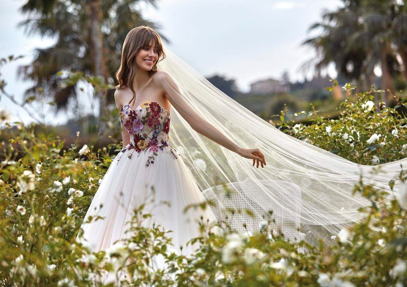 Braut in weißem Brautkleid mit langem Schleier durch eine hohe Blumenwiese laufend