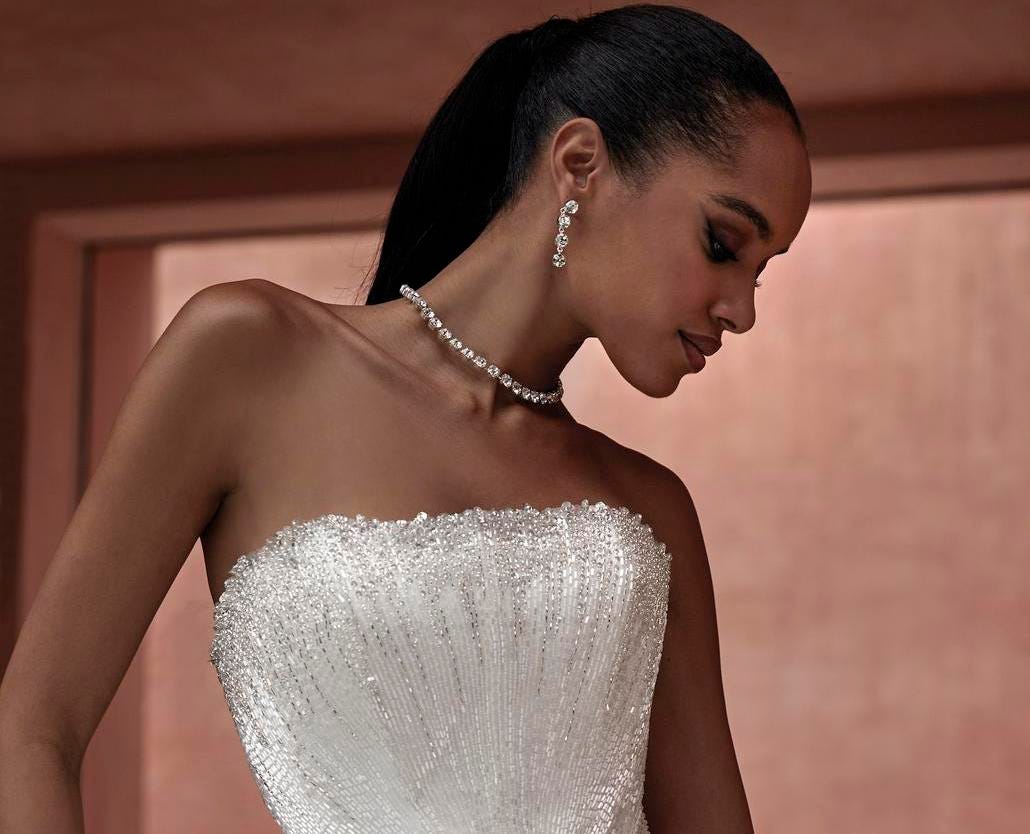 Woman with hair in a high ponytail wearing a strapless wedding dress with feather detailing on the bodice