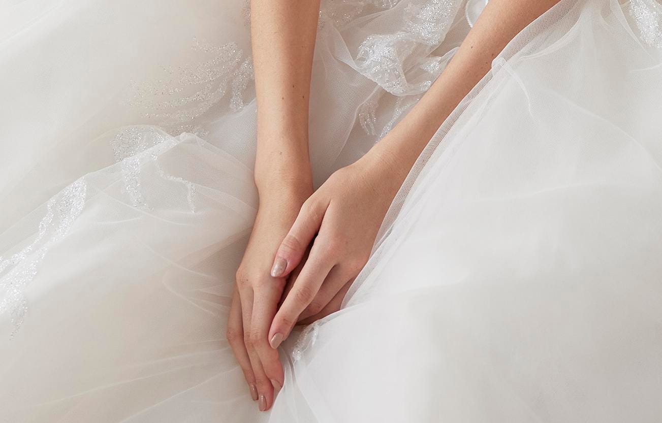 Hände einer Braut mit cremefarbenen Nägeln auf einem Brautkleid aus Tüll