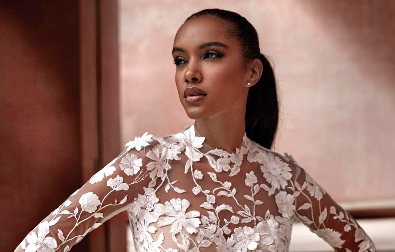 Brunette wearing a ponytail in an A-line tulle bridal dress with high neck and long sleeves, looking to the side.