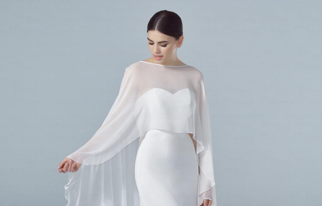 Brunette wearing a strapless bridal gown with a delicate wedding cape, gazing down at her outfit