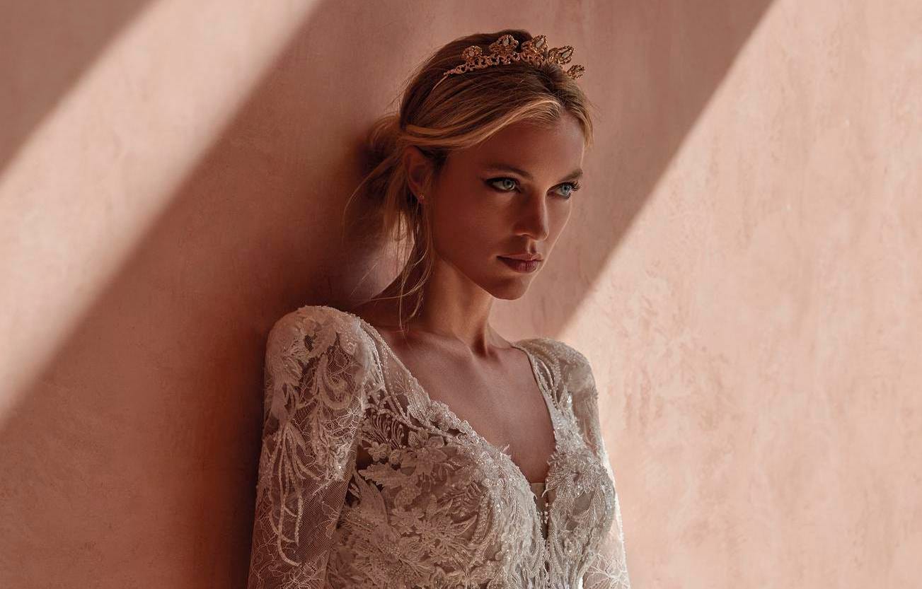 Bride with natural bride make up in a lace wedding dress leaning against a wall