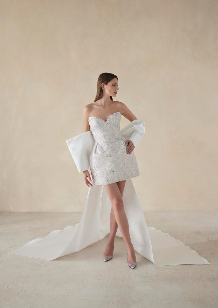 Mujer vestida con un vestido de novia mini mirando al lado con una capa sobre sus brazos