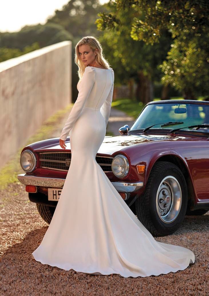 Noiva posa junto ao carro dos noivos com vestido sereia simples, com cauda, mangas longas e penteado cabelos soltos