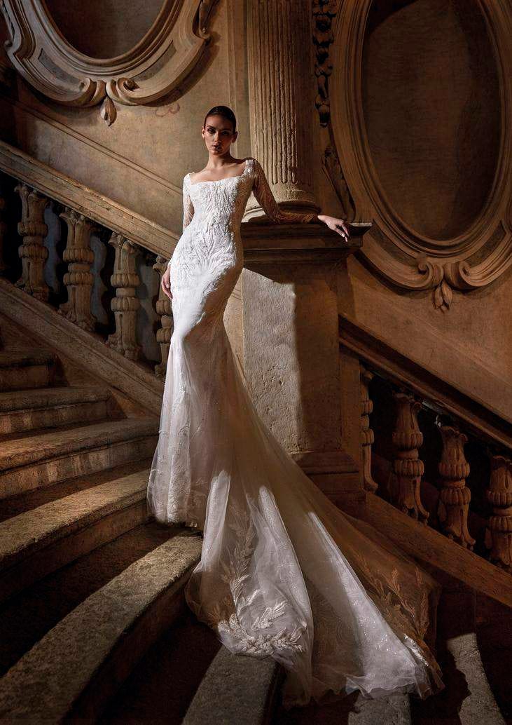 Donna su scalinata che indossa un lungo abito da sposa ricamato a maniche lunghe con strascico.