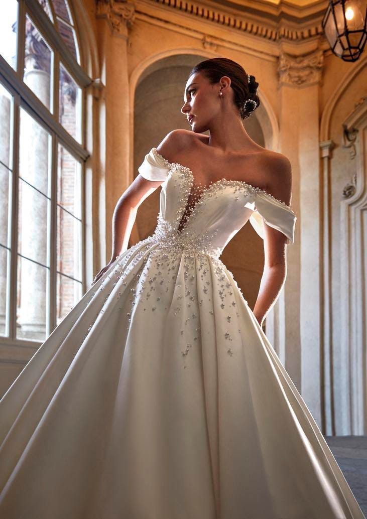 Noiva usando um vestido branco com pérolas conjugado com um penteado de coque baixo também ele adornado com pérolas