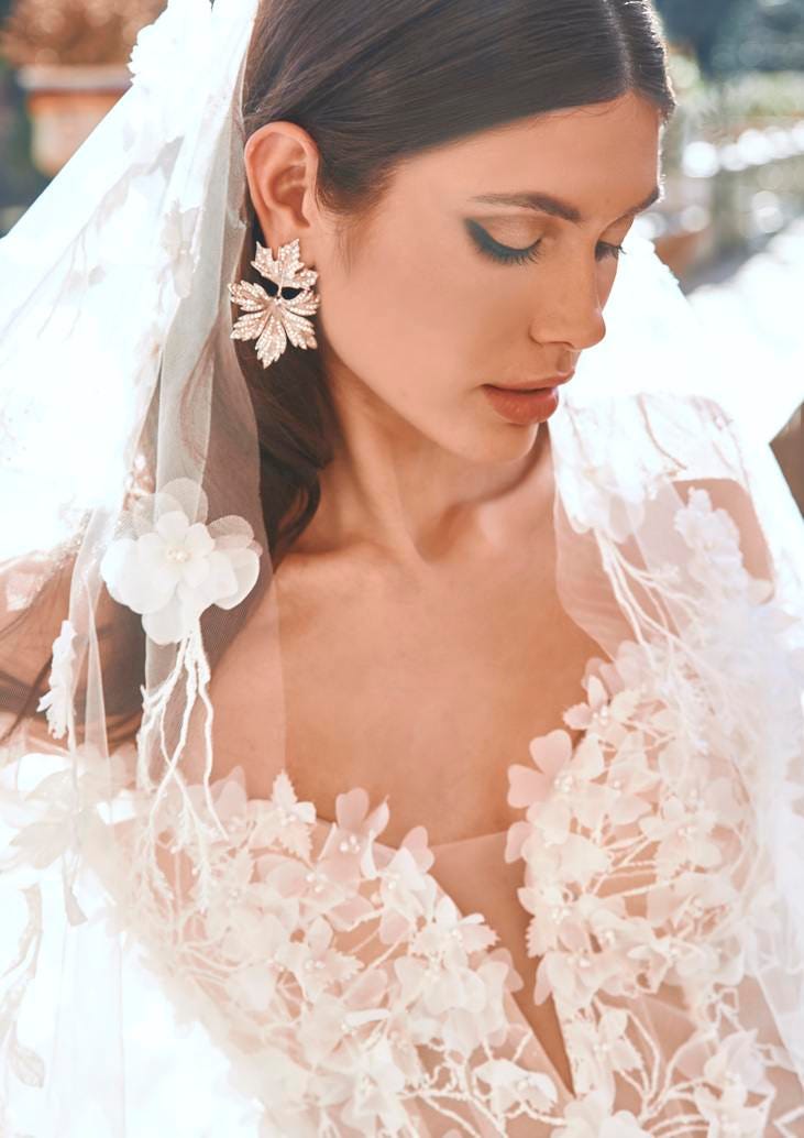 Woman with smokey wedding makeup and leaf earrings, wearing an embroidered bridal dress and veil