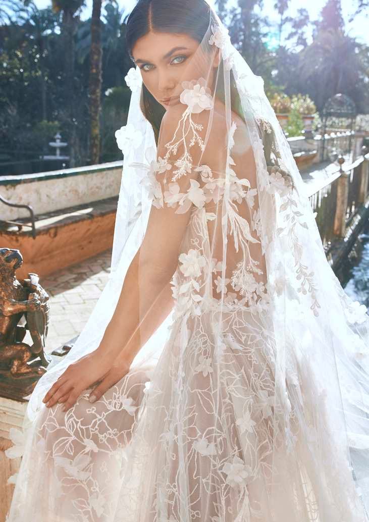 Modella in primo piano che indossa un abito da sposa in tulle trasparente con decorazioni floreali e velo da sposa