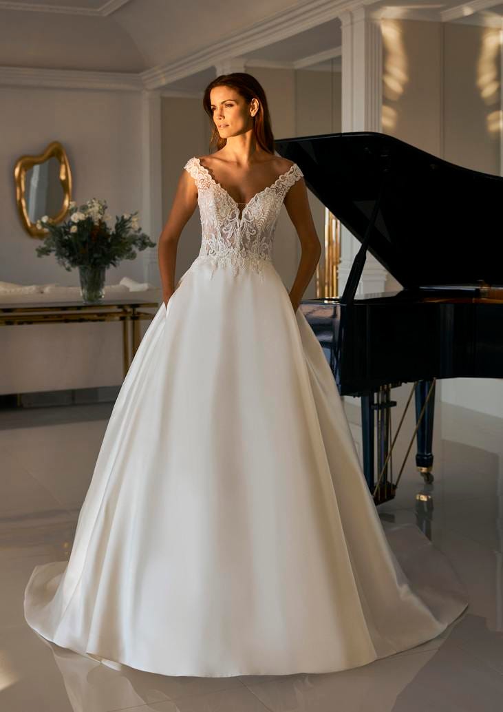 Panna młoda w sukni ślubnej typu księżniczka stojąca przy czarnym fortepianie z rękami schowanymi w kieszeniach sukni