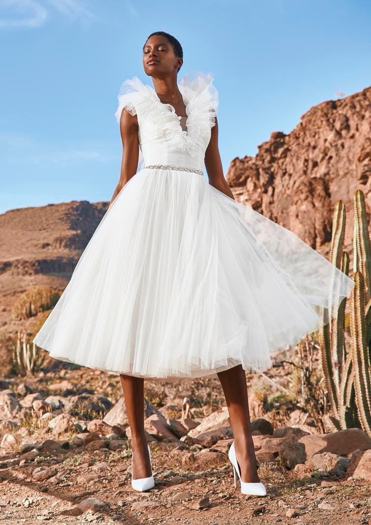 Frau mit Kurzhaarfrisur in kurzem Tüllbrautkleid und hohen weißen Schuhen in einer Wünstenlandschaft