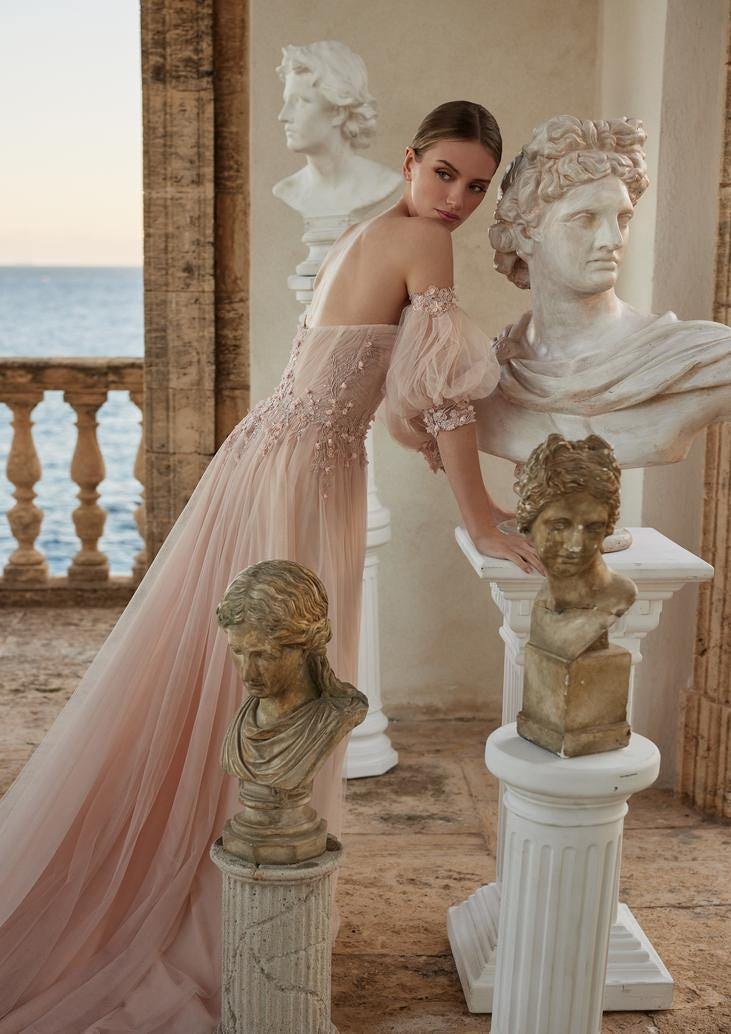 Mujer vestida con un vestido de novia rosa con flores apoyada sobre unas estatuas