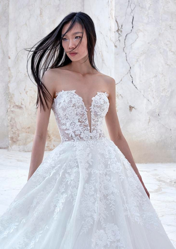 Brunette wearing a strapless lace wedding dress with a sweetheart neckline, standing outside and looking to the side