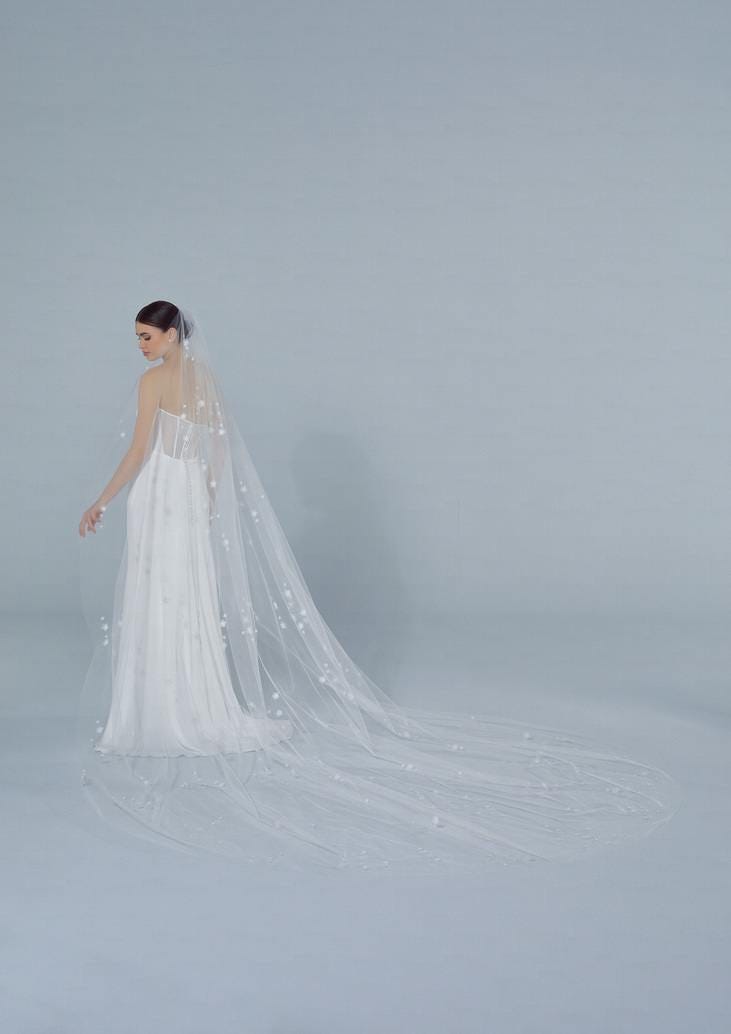 Woman in a bridal gown with an off-white wedding veil, featuring petite flowers and an extra-long train