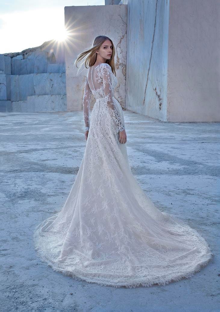 Woman wearing a two-piece lace wedding gown with delicate long sleeves and a sensual button seam, standing outside