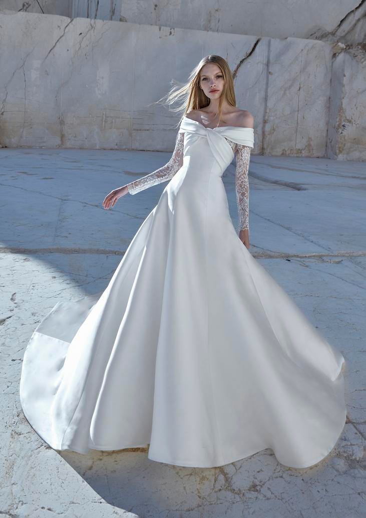 Blonde wearing a princess bridal dress with long sleeves in Mikado and sensual lace, standing outside