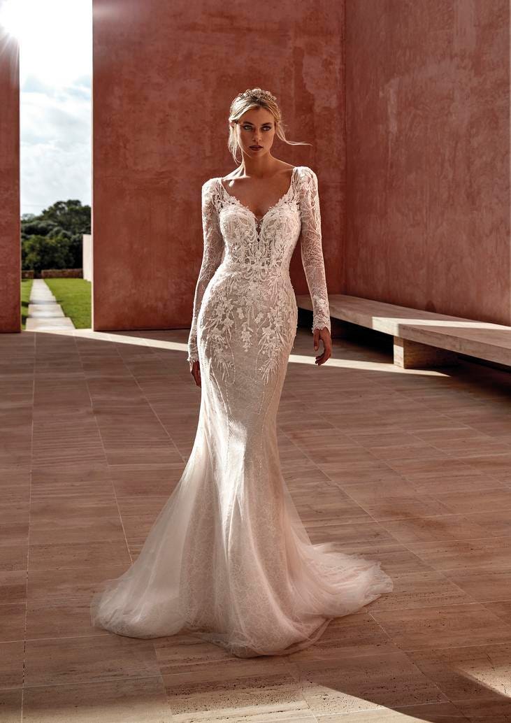 Blonde wearing a tulle mermaid wedding gown with long sleeves and V-neck, walking outside