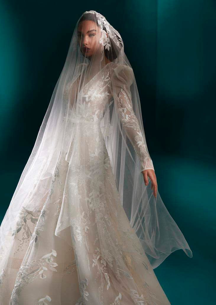 Frau mit braunen Haaren, trägt ein Brautkleid mit Blumen geschlückt und unter einem Schleier und schaut in die Ferne mit offenem Mund. 