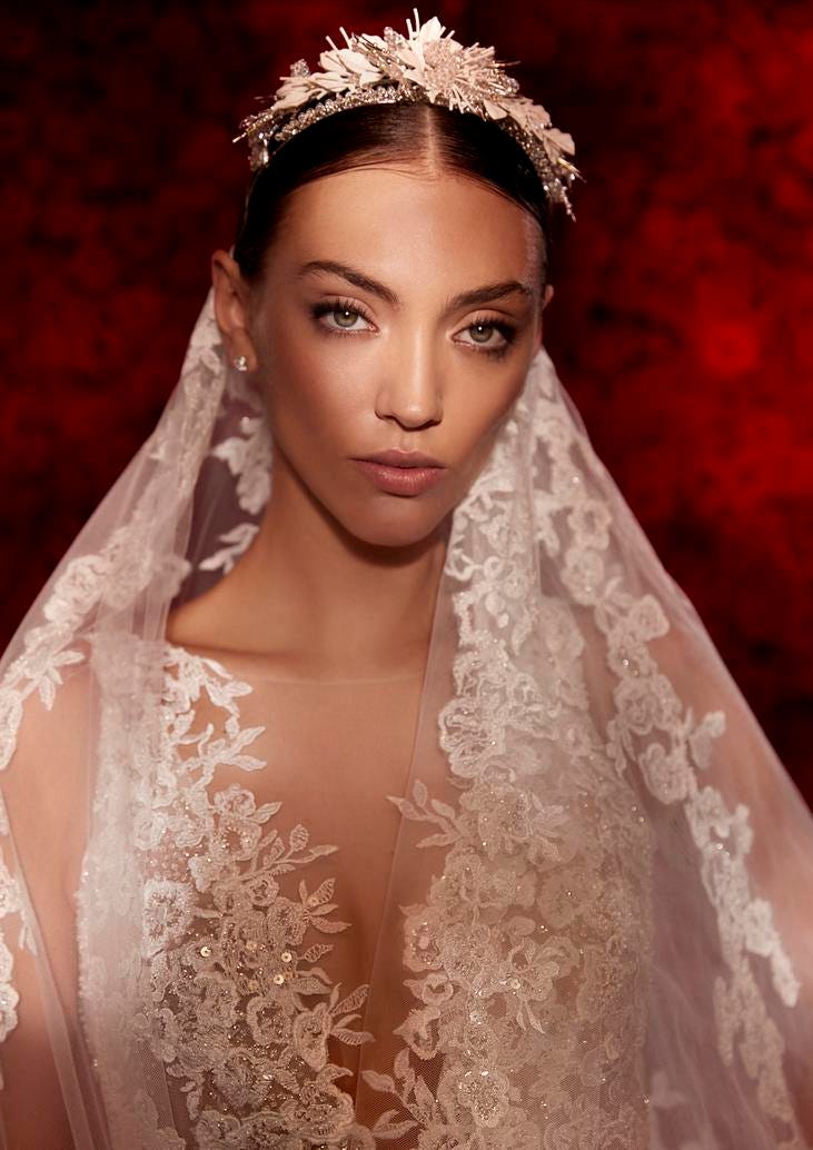 Woman wearing an embroidered mermaid wedding dress with a veil, standing against a vibrant red background